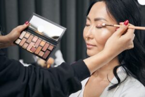 Unrecognized makeup artist doing makeup with set of eyeshadow in salon